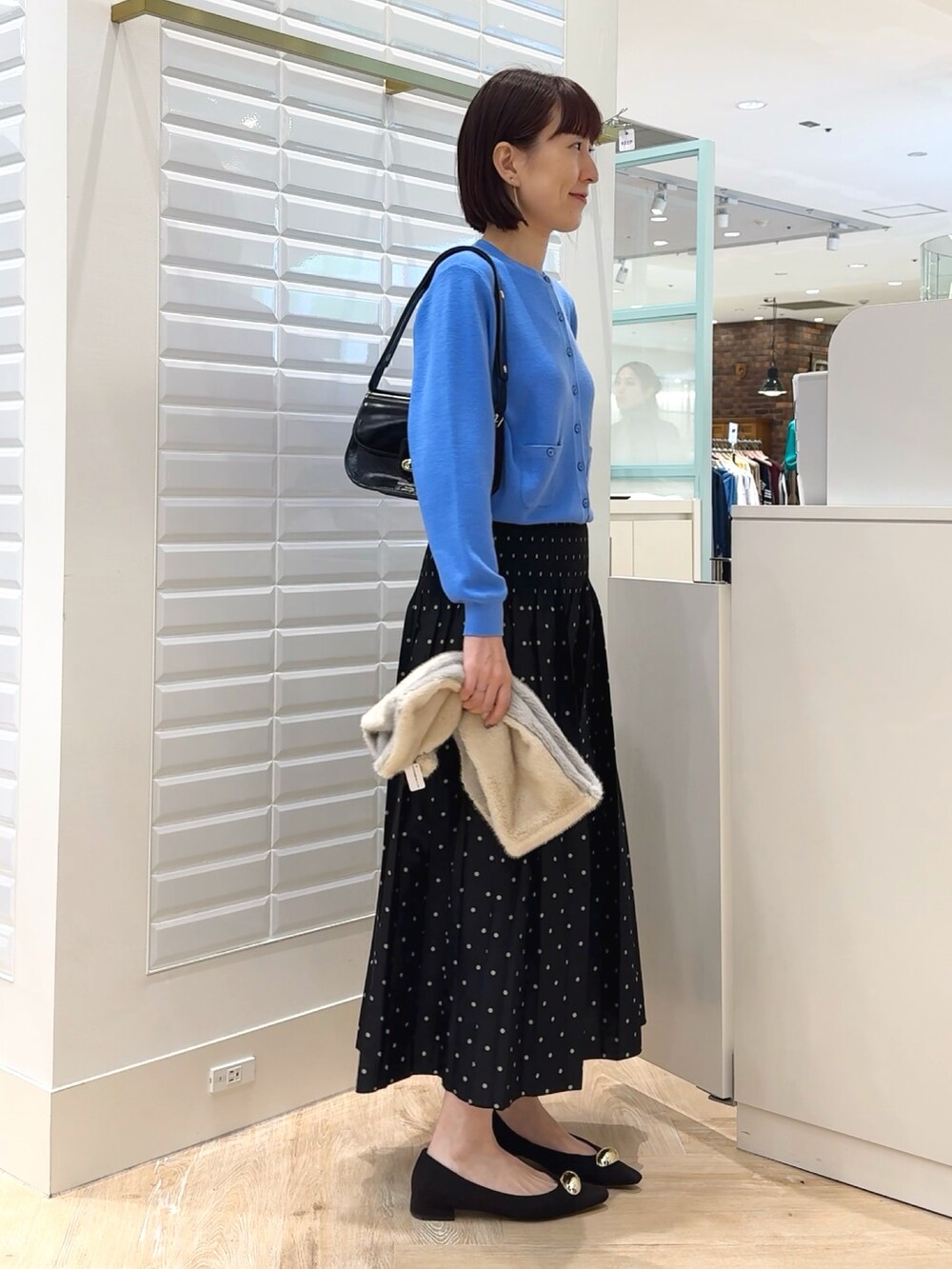 ブラック系のショルダーバッグ、ブルー系のカーディガン/ボレロ、ブラック系のスカートを着用したレディースの秋コーディネートの3枚目の写真