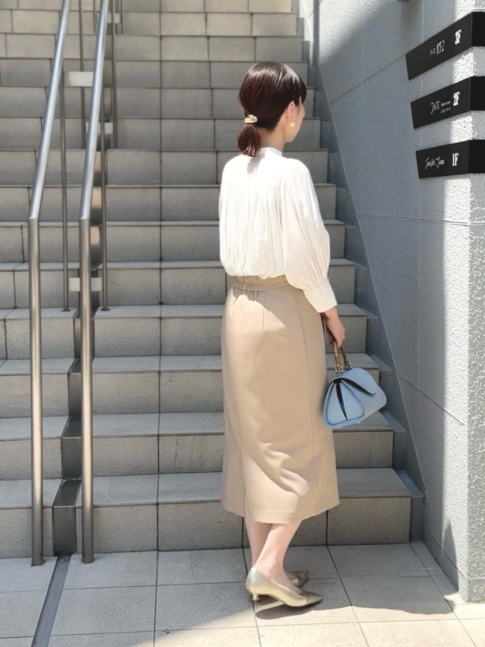 ブルー系のショルダーバッグ、ゴールド系のパンプス、ベージュ系のスカートを着用したレディースの春コーディネートの3枚目の写真