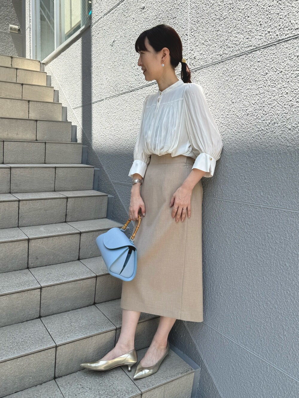 ブルー系のショルダーバッグ、ゴールド系のパンプス、ベージュ系のスカートを着用したレディースの春コーディネートの4枚目の写真