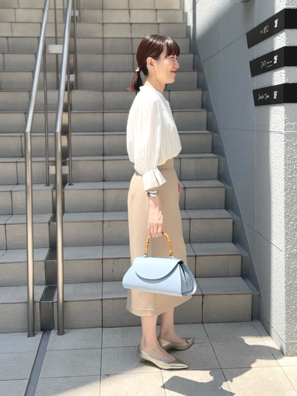 ブルー系のショルダーバッグ、ゴールド系のパンプス、ベージュ系のスカートを着用したレディースの春コーディネートの2枚目の写真