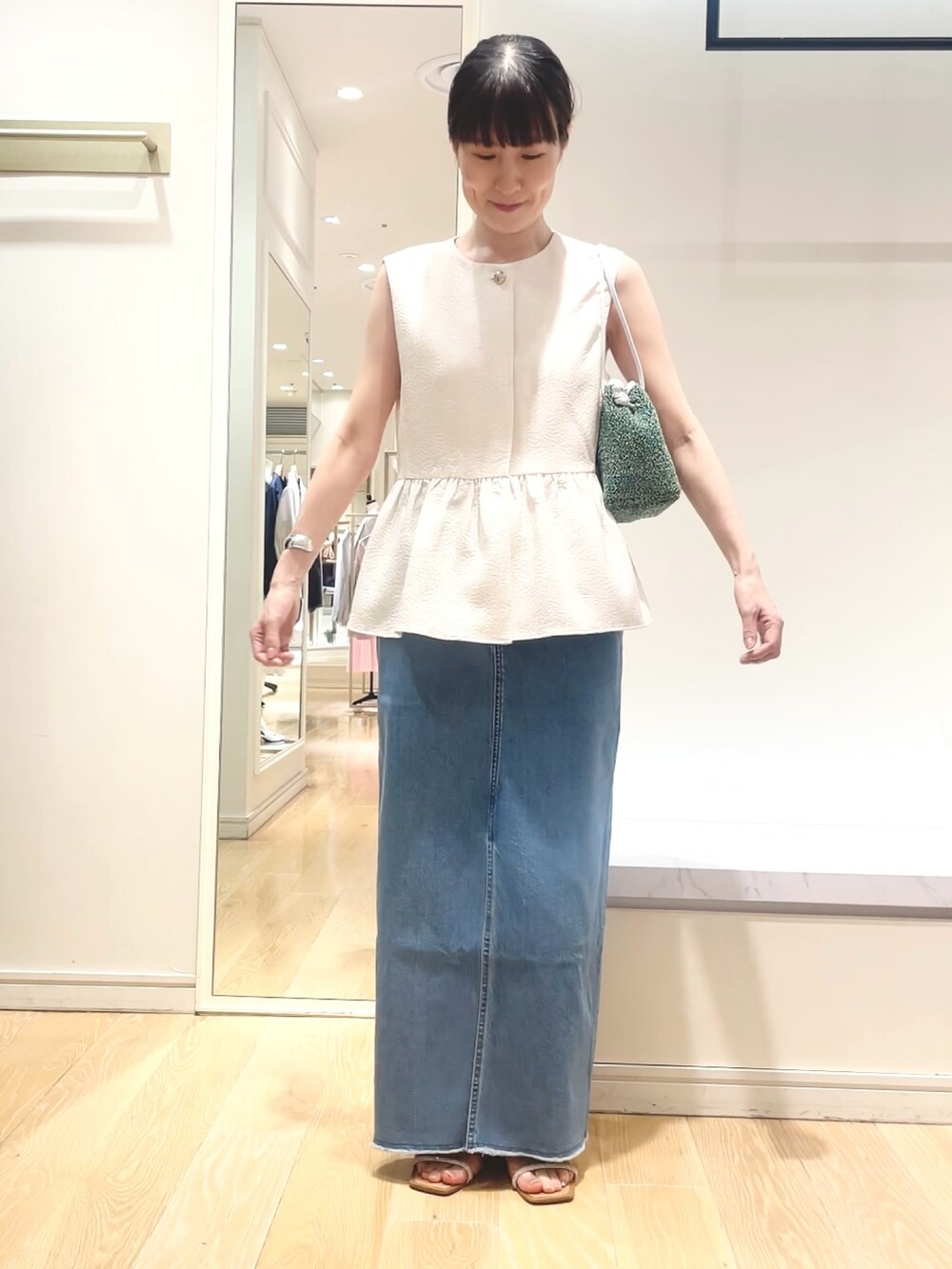 ホワイト系のベスト、グリーン系のショルダーバッグ、ブルー系のデニムスカートを着用したレディースの春コーディネートの7枚目の写真