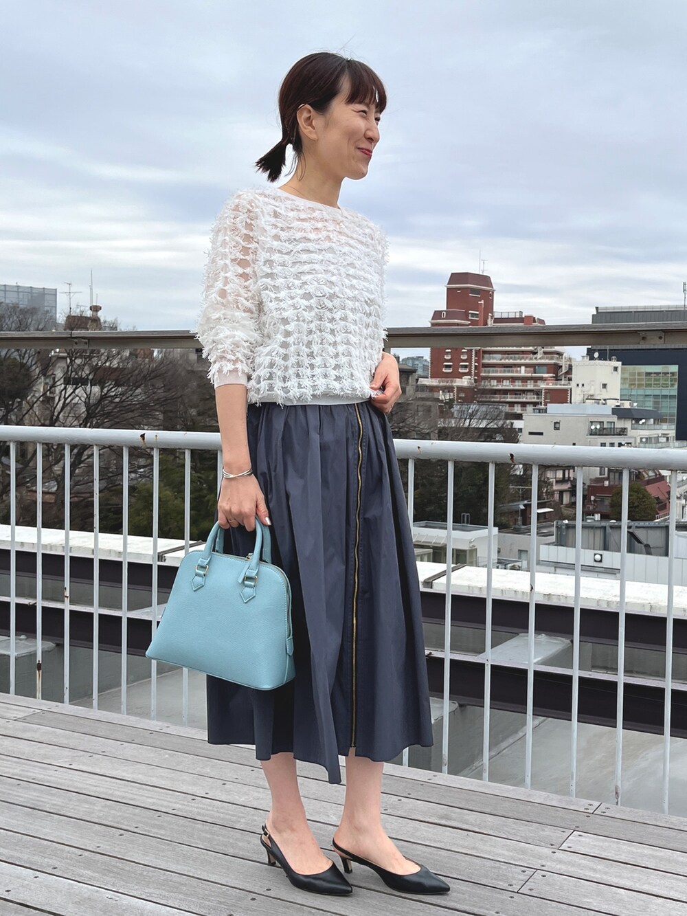 ブルー系のボストンバッグ、ブラック系のパンプス、グレー系のスカートを着用したレディースの冬コーディネートの7枚目の写真