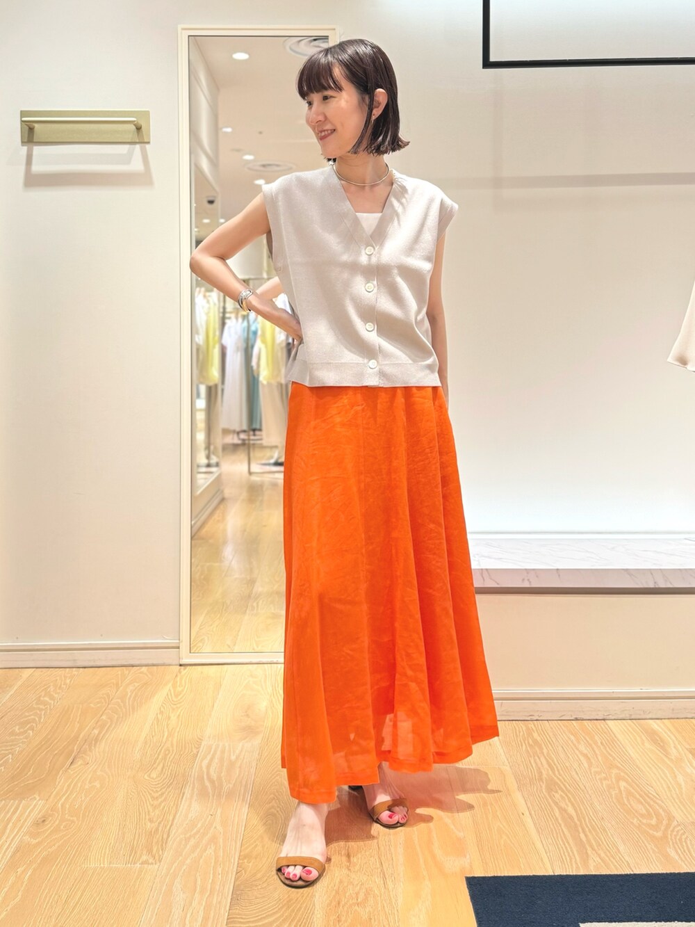 ベージュ系のベスト、ホワイト系のタンクトップ、オレンジ系のスカートを着用したレディースの夏コーディネートの4枚目の写真