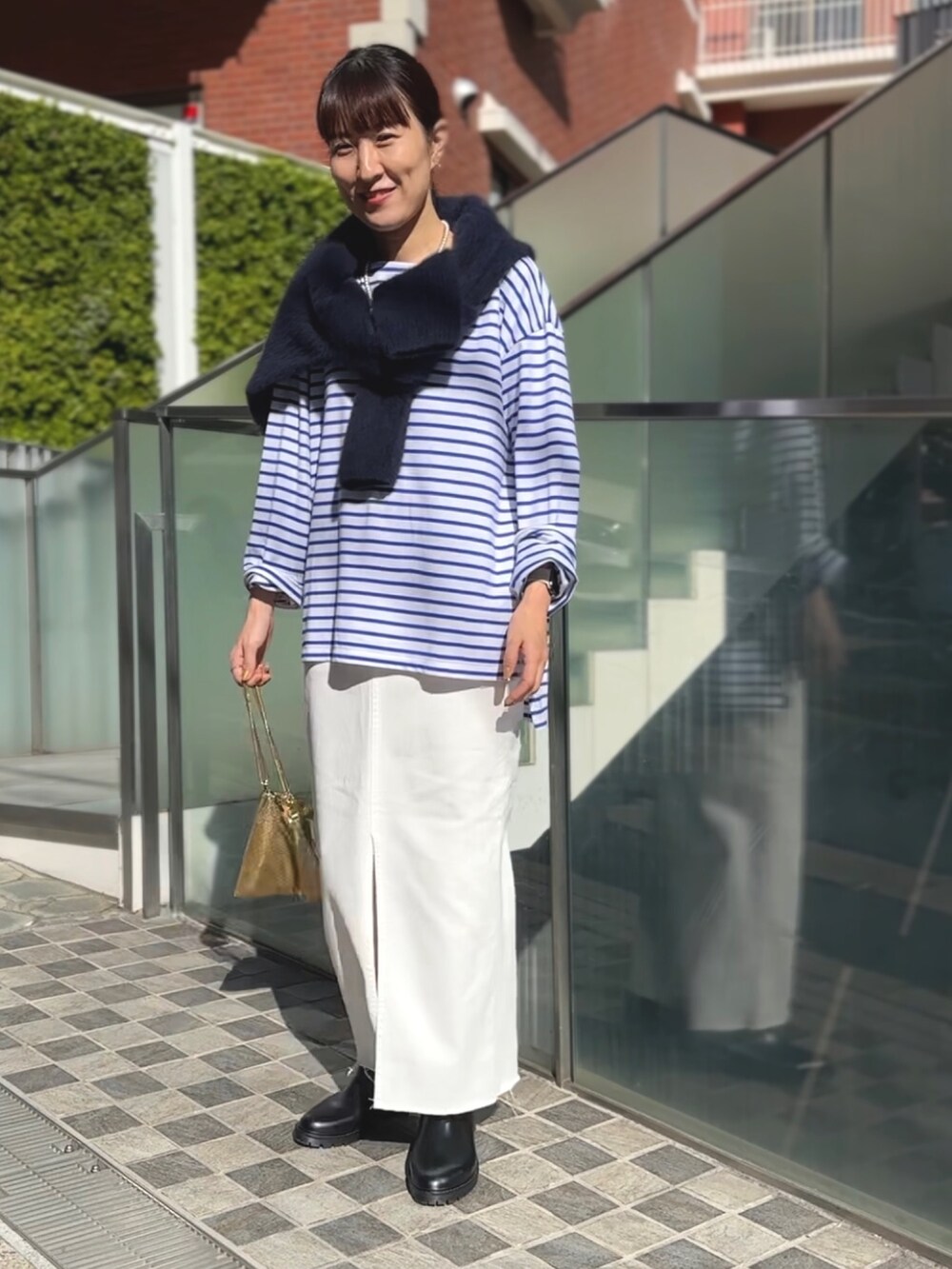 ゴールド系のクラッチバッグ、ブラック系のブーツ、ホワイト系のデニムスカートを着用したレディースの冬コーディネートの5枚目の写真