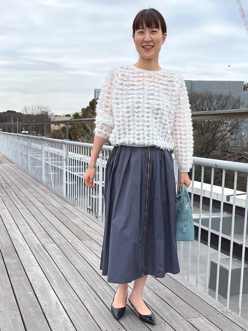 ブルー系のボストンバッグ、ブラック系のパンプス、グレー系のスカートを着用したレディースの冬コーディネートの2枚目の写真