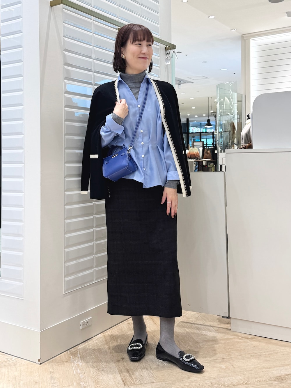 グレー系のニット/セーター、ベージュ系のスカート、ブルー系のショルダーバッグを着用したレディースの秋コーディネートの6枚目の写真