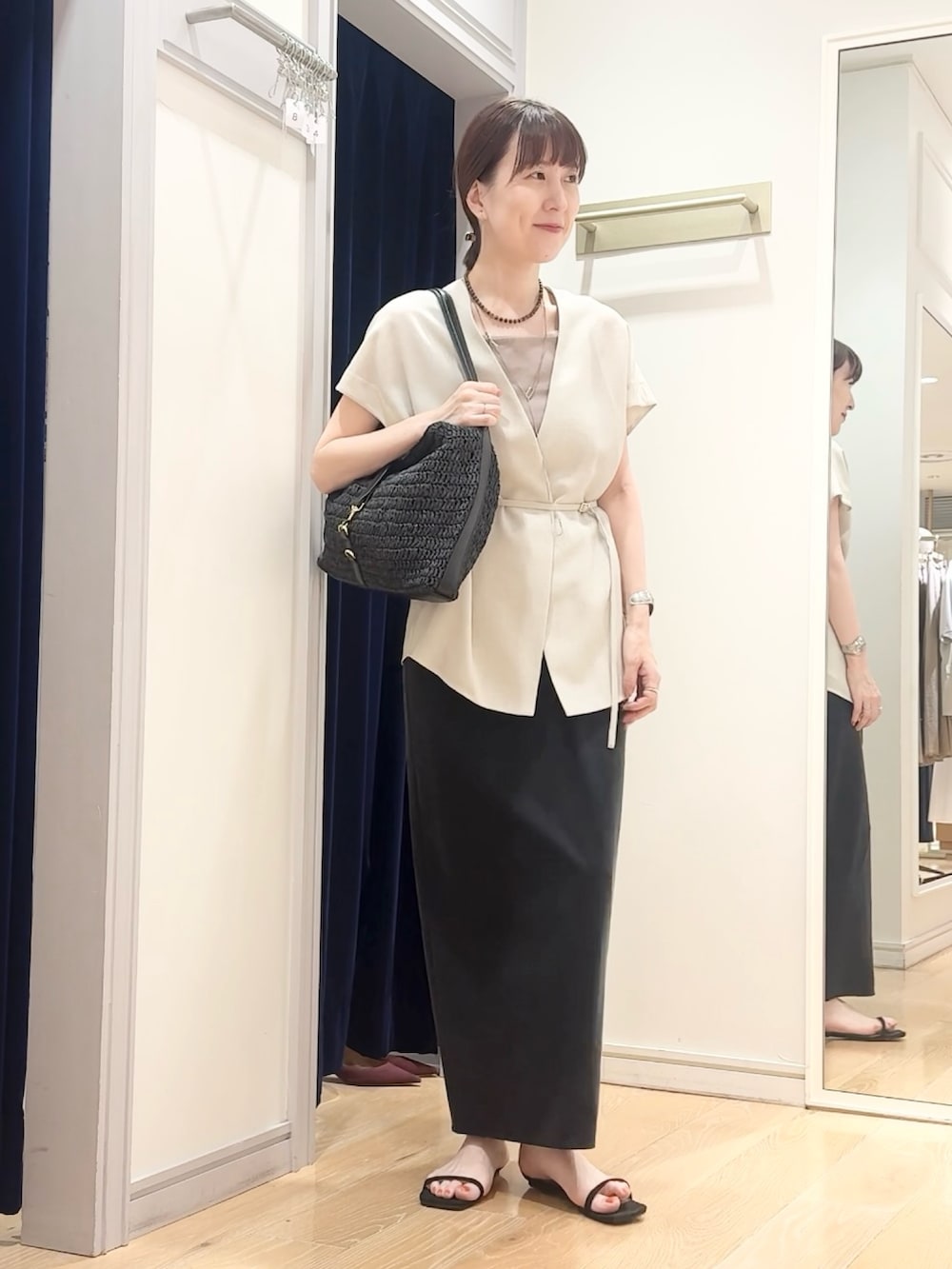 ブラック系のスカート、ブラック系のショルダーバッグ、ベージュ系のタンクトップを着用したレディースの夏コーディネートの2枚目の写真
