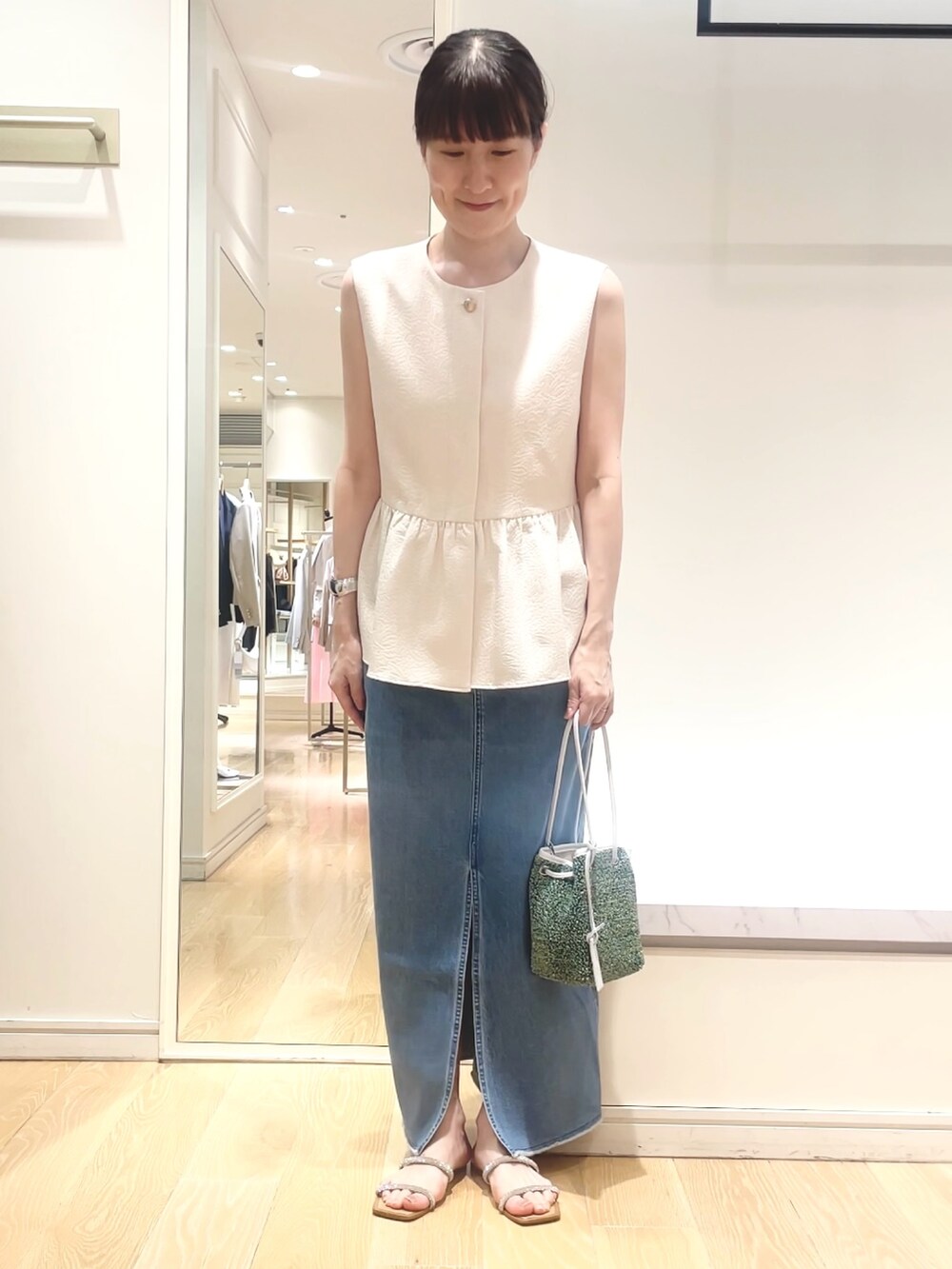 ホワイト系のベスト、グリーン系のショルダーバッグ、ブルー系のデニムスカートを着用したレディースの春コーディネートの9枚目の写真