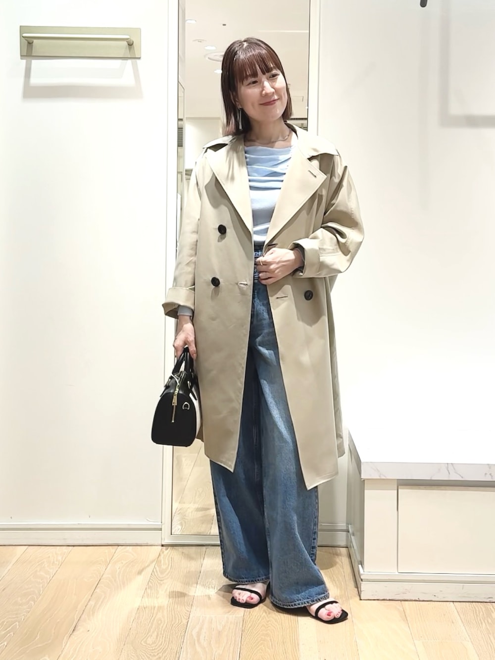 ブラック系のボストンバッグ、ブルー系のニット/セーター、ベージュ系のトレンチコートを着用したレディースの春コーディネートの2枚目の写真