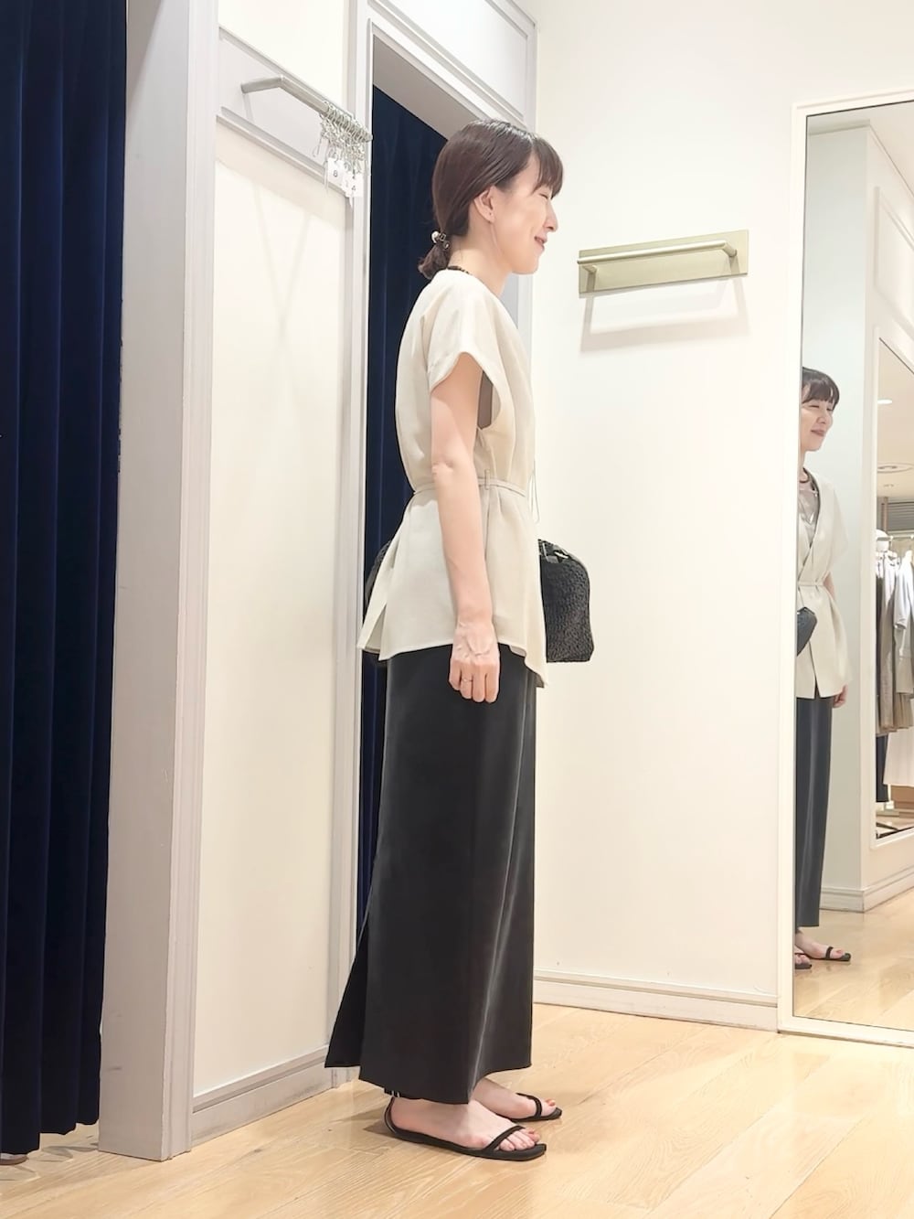 ブラック系のスカート、ブラック系のショルダーバッグ、ベージュ系のタンクトップを着用したレディースの夏コーディネートの4枚目の写真