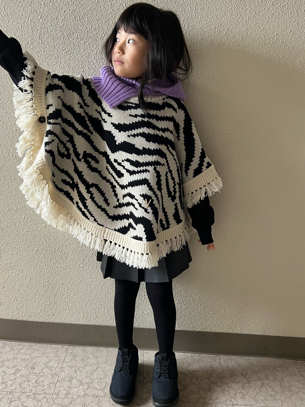 ブラック系のポンチョ、ブラック系のスカート、ブラック系のブーツを着用したキッズの冬コーディネートの3枚目の写真