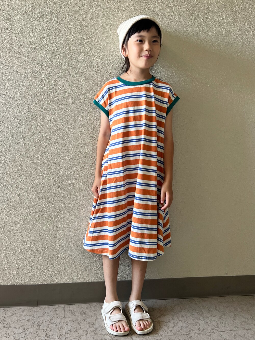 オレンジ系のワンピース、ベージュ系のサンダル、ホワイト系のキャップを着用したキッズの夏コーディネートの4枚目の写真