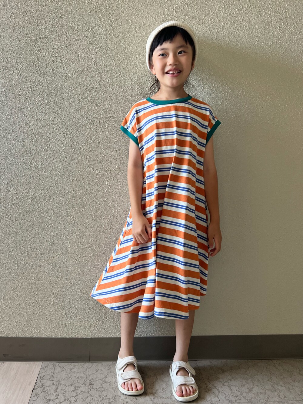 オレンジ系のワンピース、ベージュ系のサンダル、ホワイト系のキャップを着用したキッズの夏コーディネートの3枚目の写真