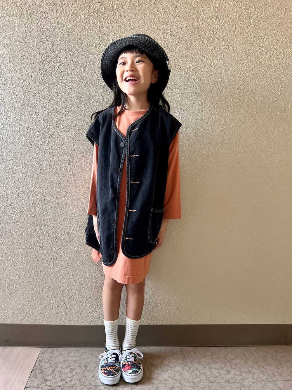 オレンジ系のワンピース、ブラック系のベスト、その他のスニーカーを着用したキッズの春コーディネートの3枚目の写真