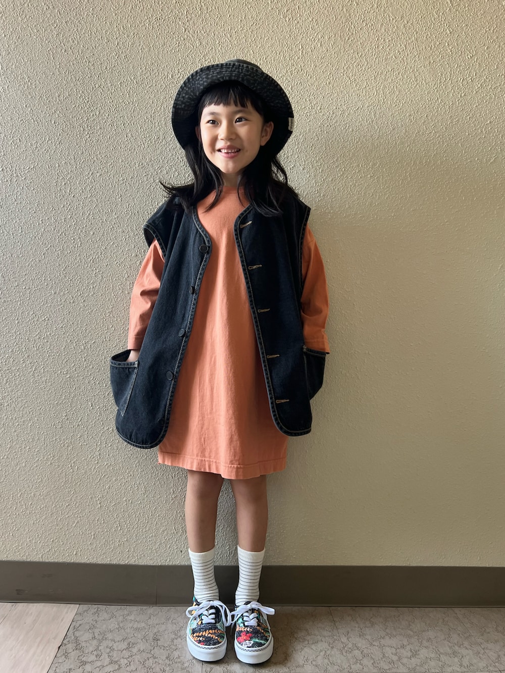 オレンジ系のワンピース、ブラック系のベスト、その他のスニーカーを着用したキッズの春コーディネートの2枚目の写真