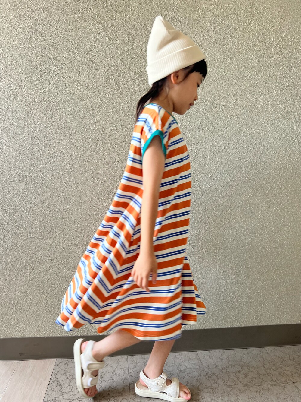オレンジ系のワンピース、ベージュ系のサンダル、ホワイト系のキャップを着用したキッズの夏コーディネートの5枚目の写真