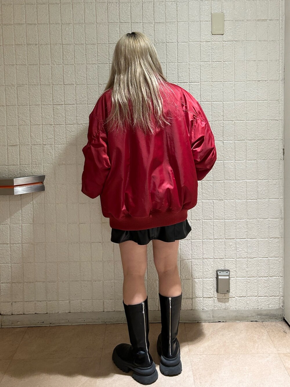 レッド系のMA-1、ブラック系のブーツ、ブラック系のジャンパースカートを着用したレディースの冬コーディネートの3枚目の写真