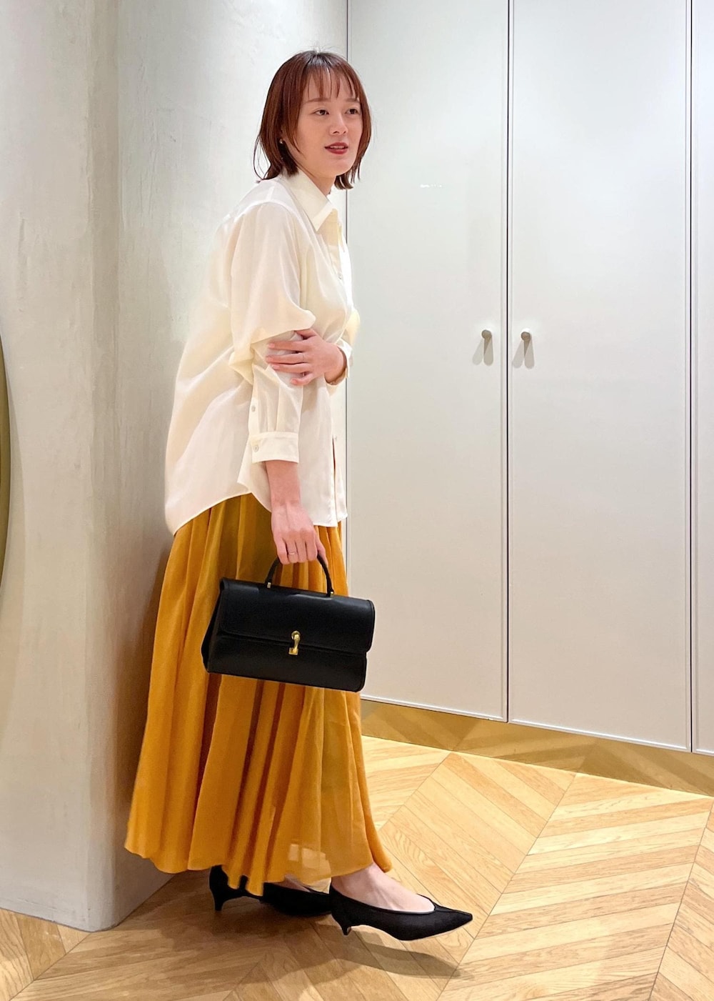 ブラック系のパンプス、オレンジ系のスカート、ホワイト系のシャツ/ブラウスを着用したレディースの春コーディネートの7枚目の写真
