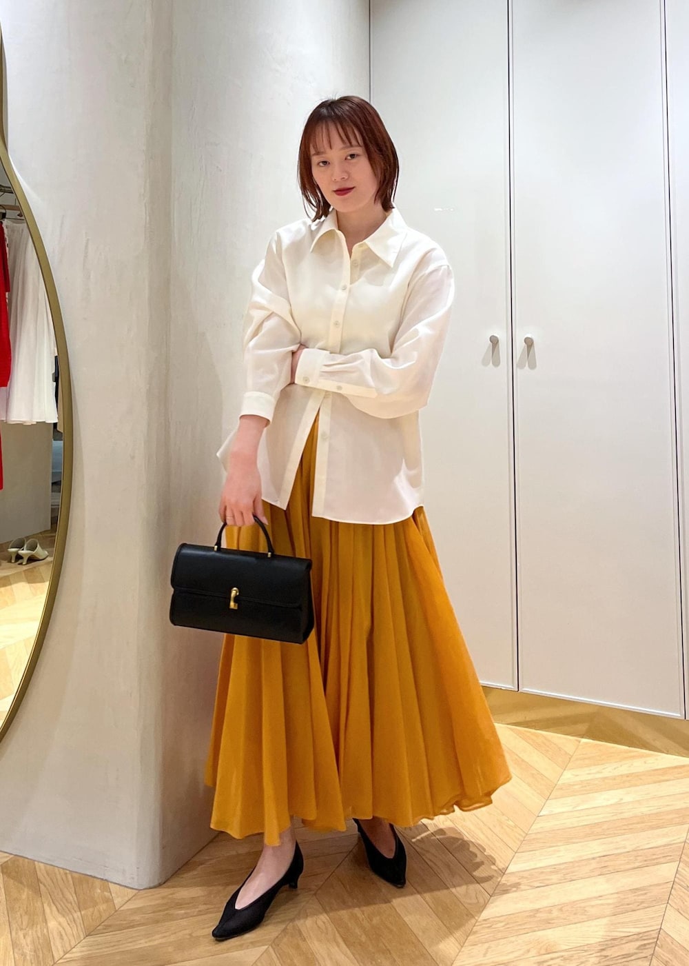 ブラック系のパンプス、オレンジ系のスカート、ホワイト系のシャツ/ブラウスを着用したレディースの春コーディネートの6枚目の写真