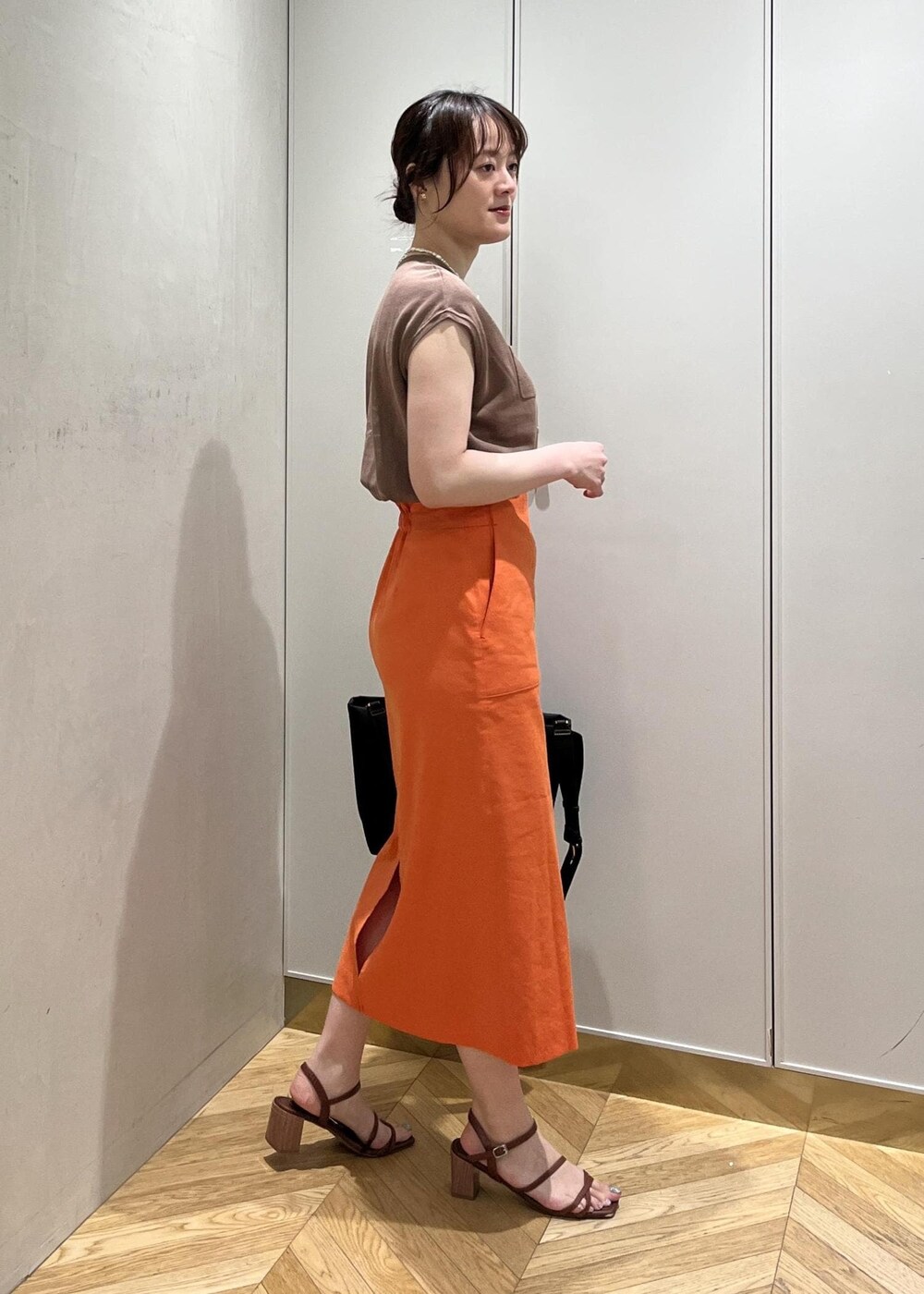 ブラック系のトートバッグ、ブラウン系のニット/セーター、オレンジ系のスカートを着用したレディースの夏コーディネートの2枚目の写真