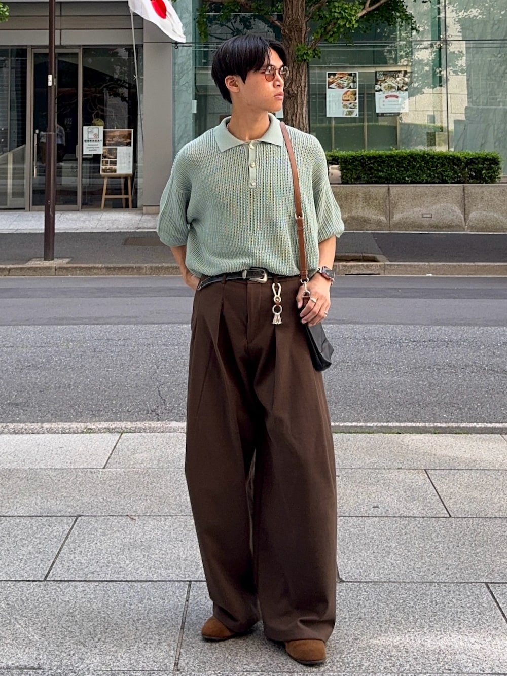 グリーン系のポロシャツ、ブラウン系のスラックス、ブラック系のショルダーバッグを着用したメンズの春コーディネートの3枚目の写真