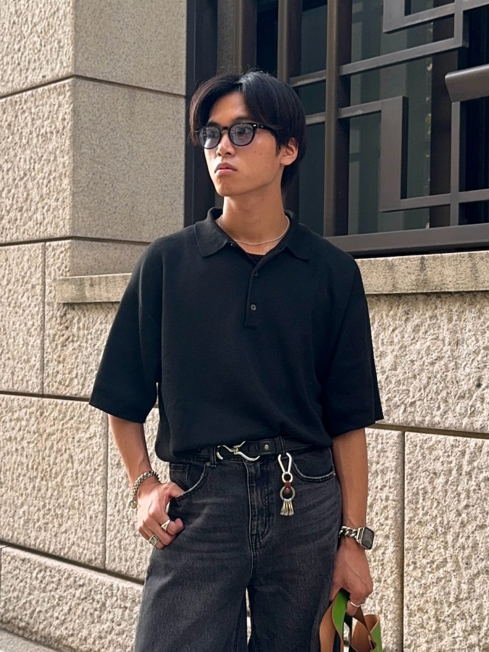 ブラック系のポロシャツ、ブラック系のデニムパンツ、グリーン系のハンドバッグを着用したメンズの夏コーディネートの2枚目の写真