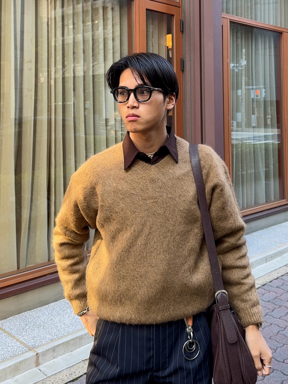 イエロー系のニット/セーター、ブラウン系のシャツ/ブラウス、ブラック系のスラックスを着用したメンズの春コーディネートの2枚目の写真