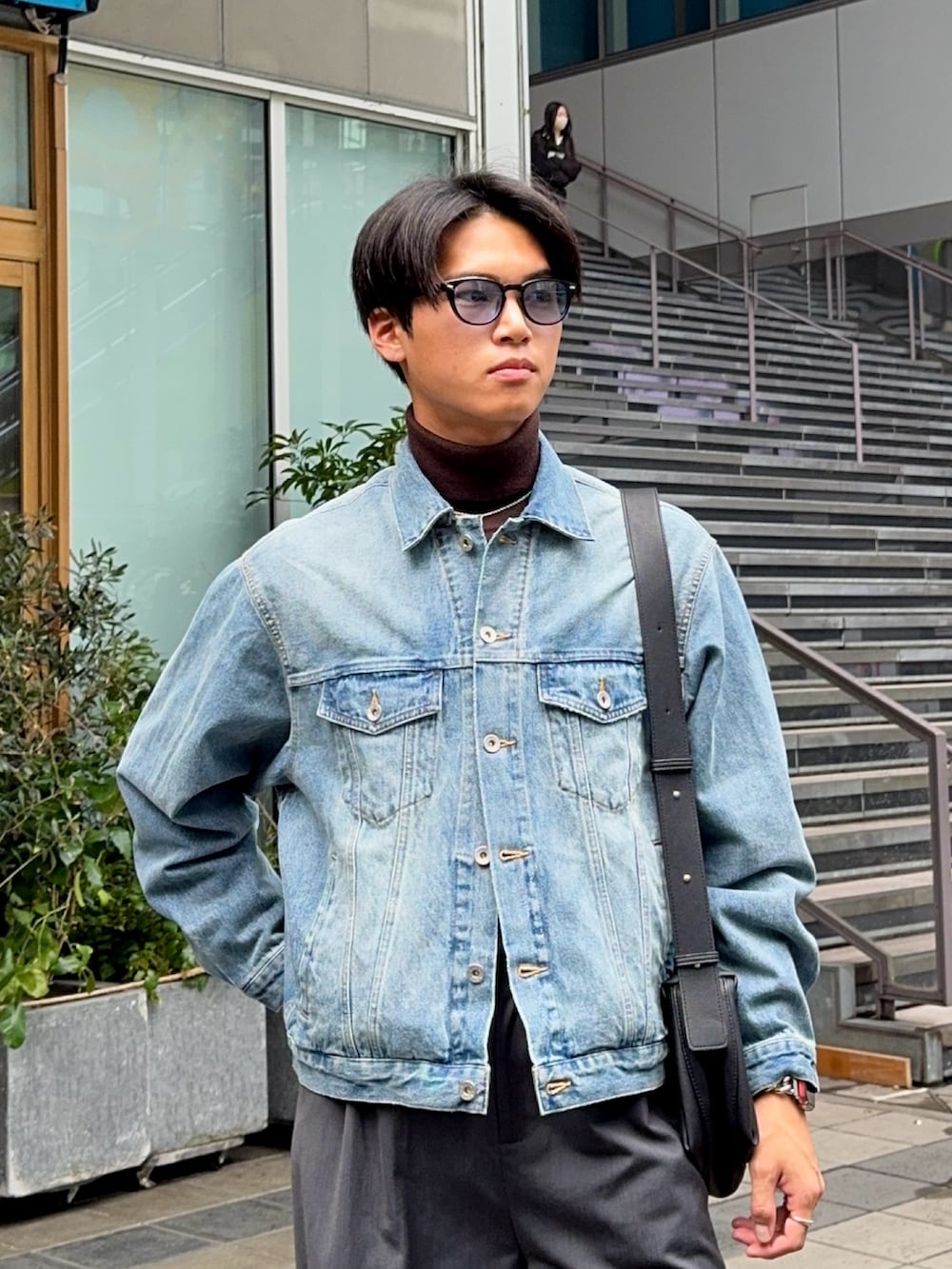 ブルー系のデニムジャケット、グレー系のスラックス、ブラック系のショルダーバッグを着用したメンズの冬コーディネートの2枚目の写真