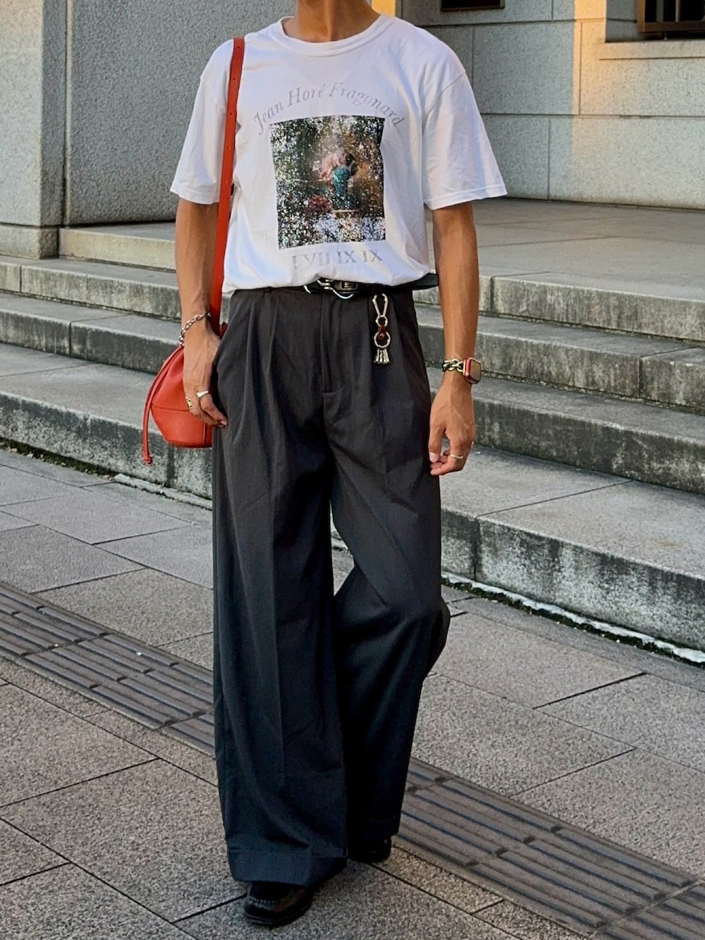 ホワイト系のTシャツ/カットソー、オレンジ系のバッグ、グレー系のスラックスを着用したメンズの夏コーディネートの4枚目の写真