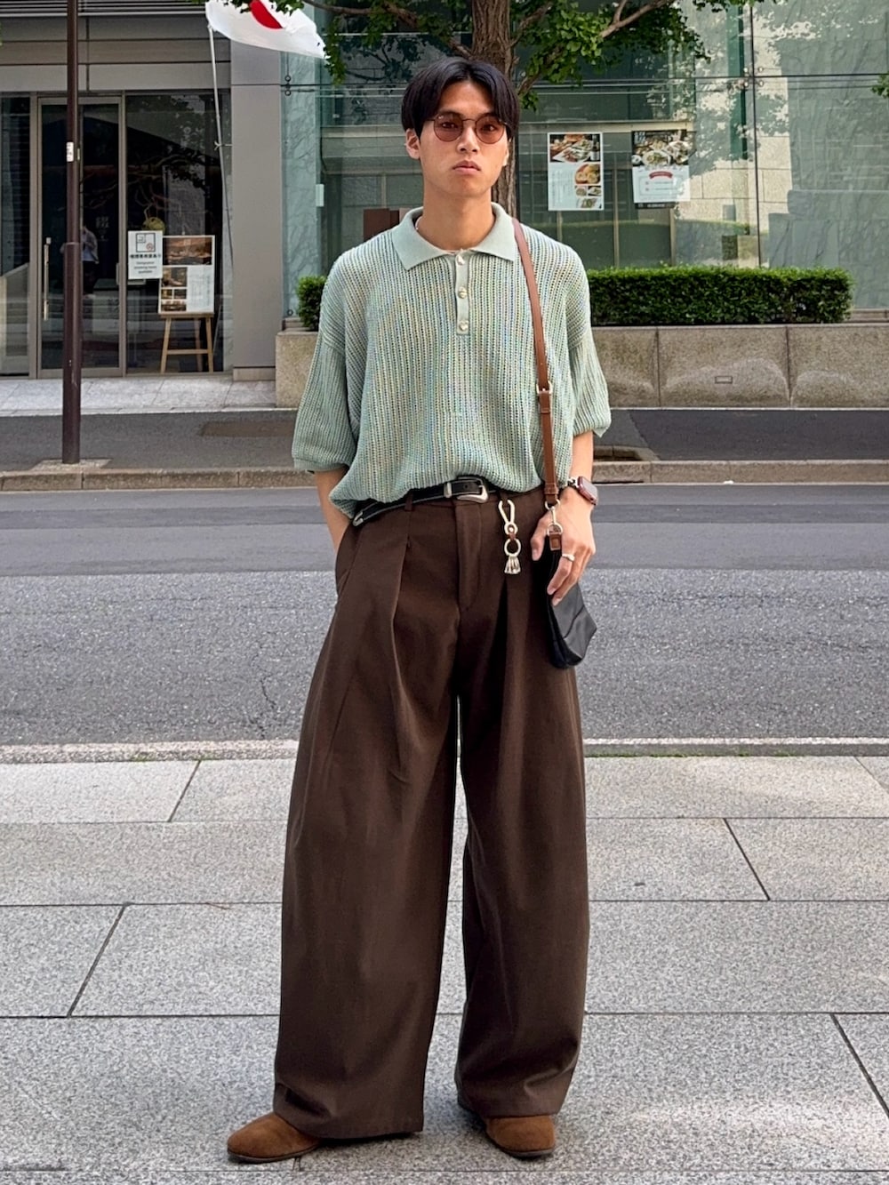 グリーン系のポロシャツ、ブラウン系のスラックス、ブラック系のショルダーバッグを着用したメンズの春コーディネートの5枚目の写真