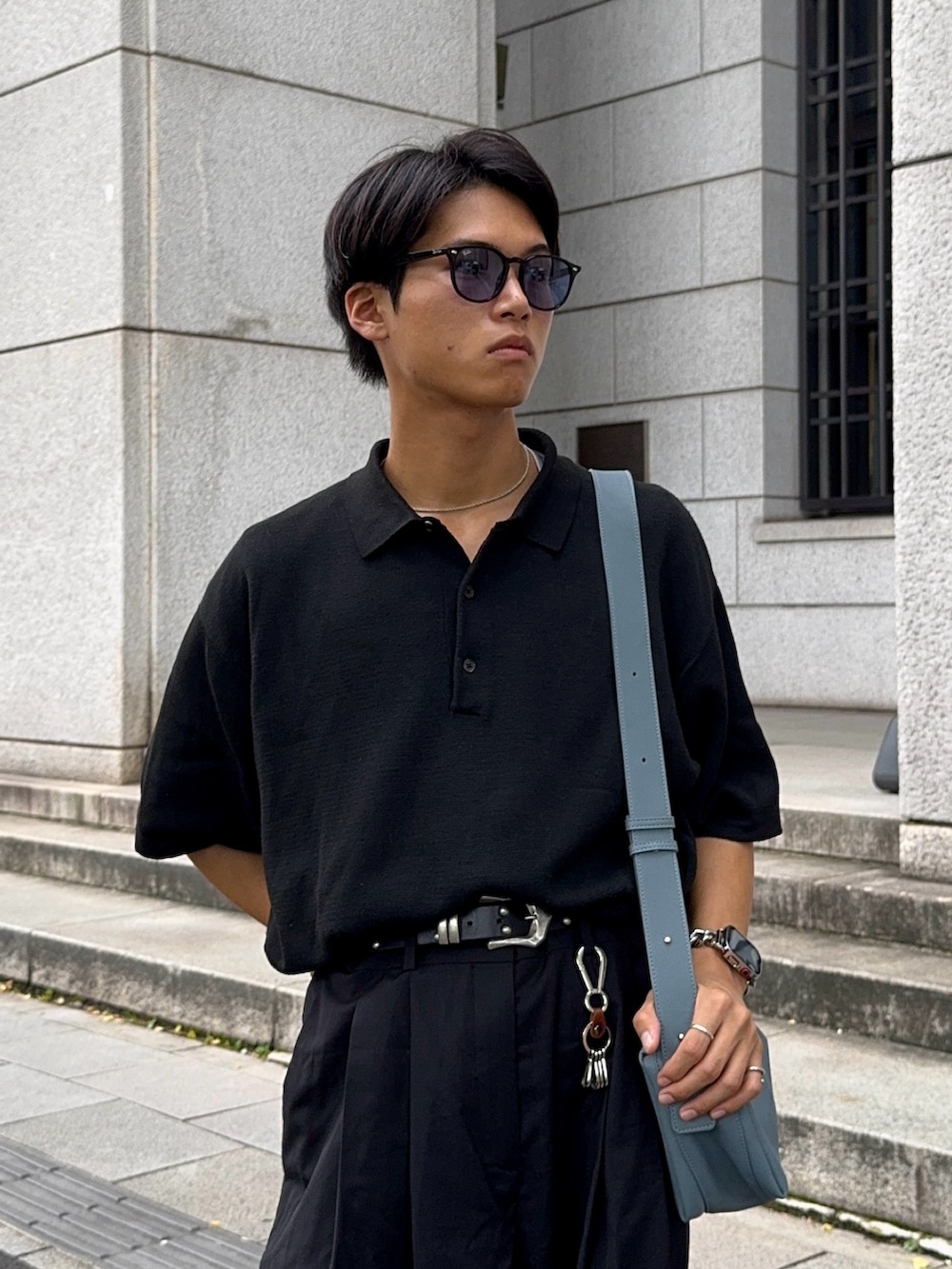 ブラック系のローファー、ブラック系のポロシャツ、ブルー系のショルダーバッグを着用したメンズの夏コーディネートの2枚目の写真