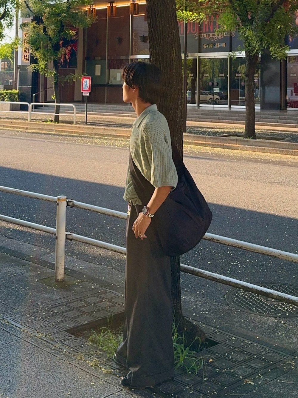 グレー系のスラックス、グリーン系のポロシャツ、ブラック系のショルダーバッグを着用したメンズの夏コーディネートの5枚目の写真