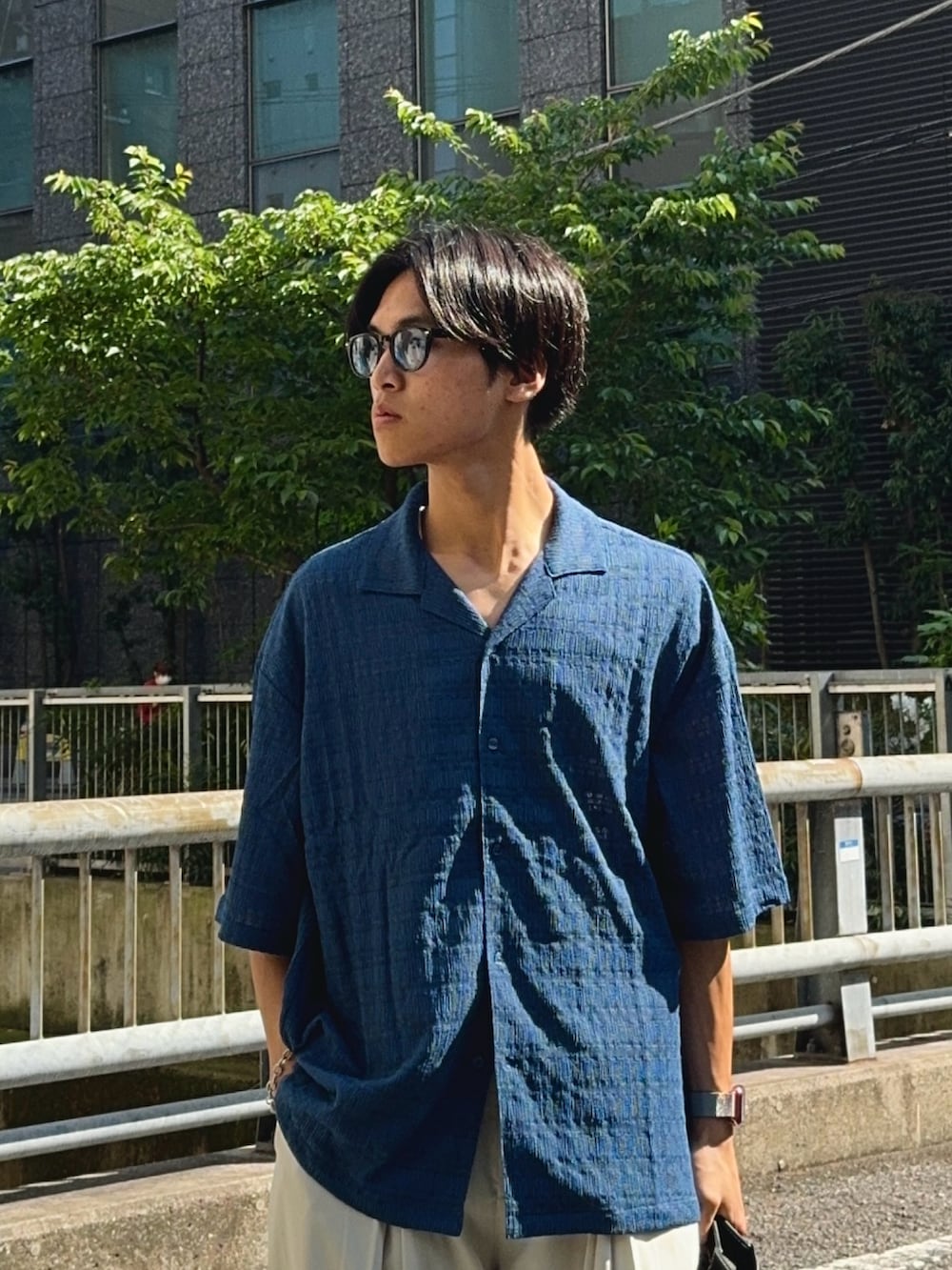 ブルー系のシャツ/ブラウス、ホワイト系のスラックス、ブラック系のハンドバッグを着用したメンズの春コーディネートの2枚目の写真