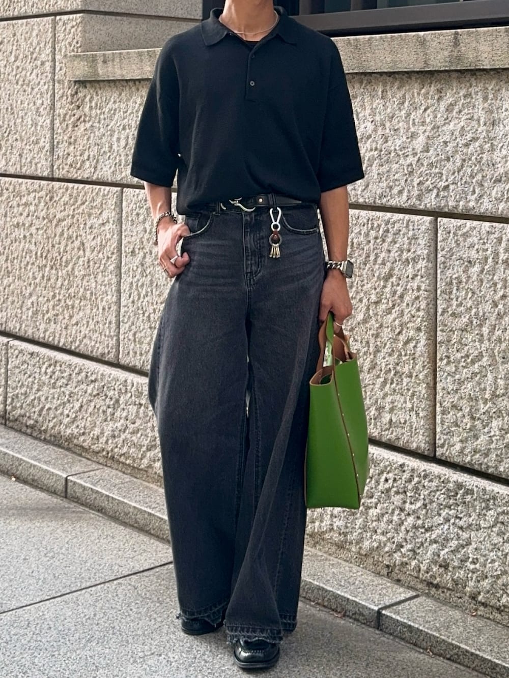 ブラック系のポロシャツ、ブラック系のデニムパンツ、グリーン系のハンドバッグを着用したメンズの夏コーディネートの4枚目の写真