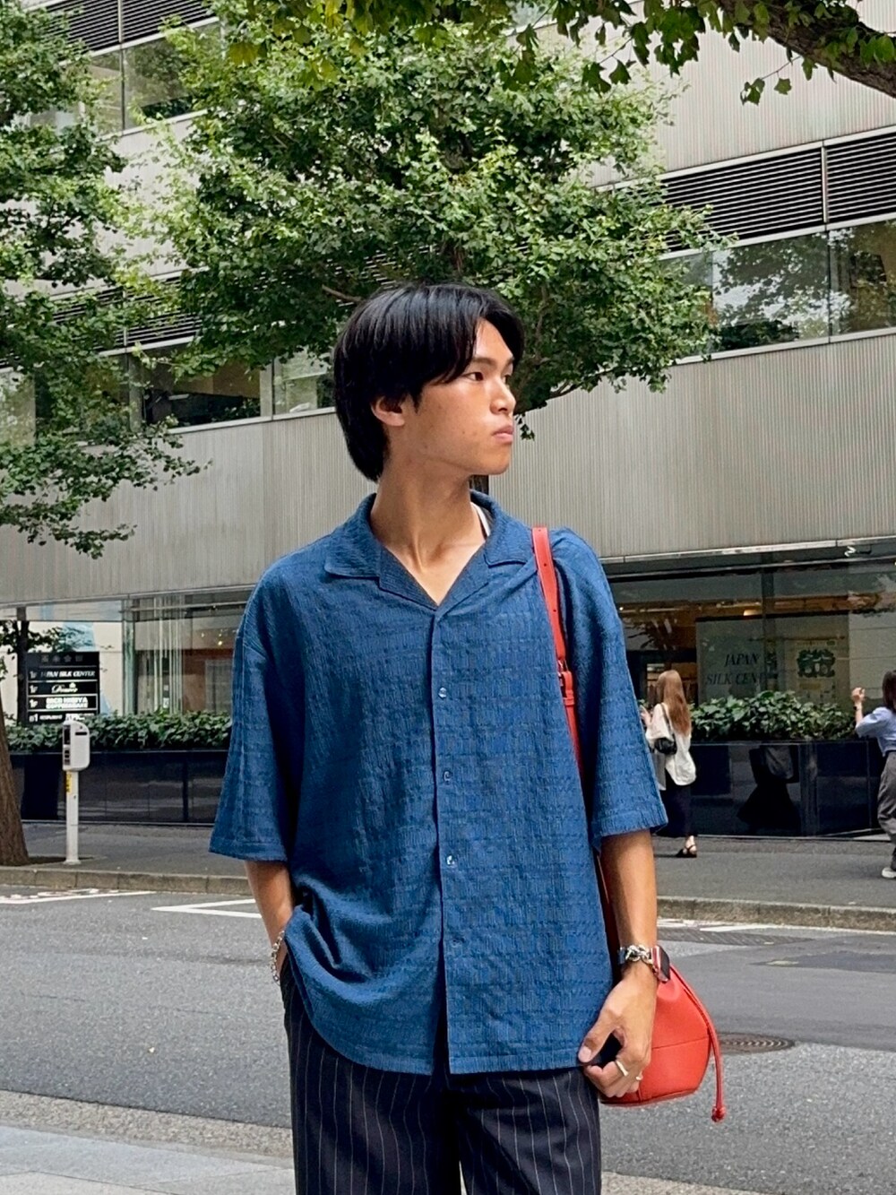 ブルー系のシャツ/ブラウス、オレンジ系のバッグ、ブラック系のスラックスを着用したメンズの夏コーディネートの2枚目の写真