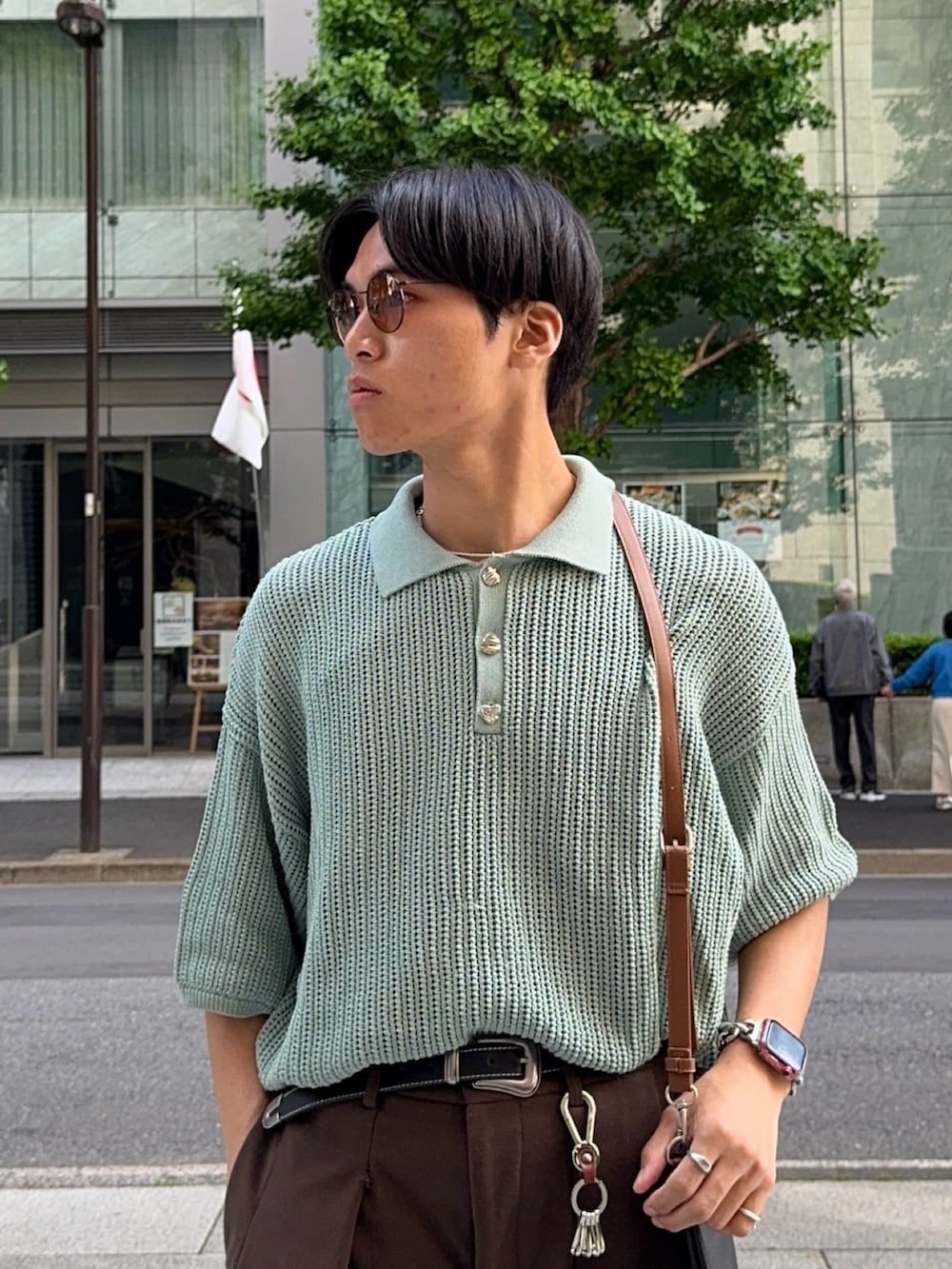 グリーン系のポロシャツ、ブラウン系のスラックス、ブラック系のショルダーバッグを着用したメンズの春コーディネートの2枚目の写真