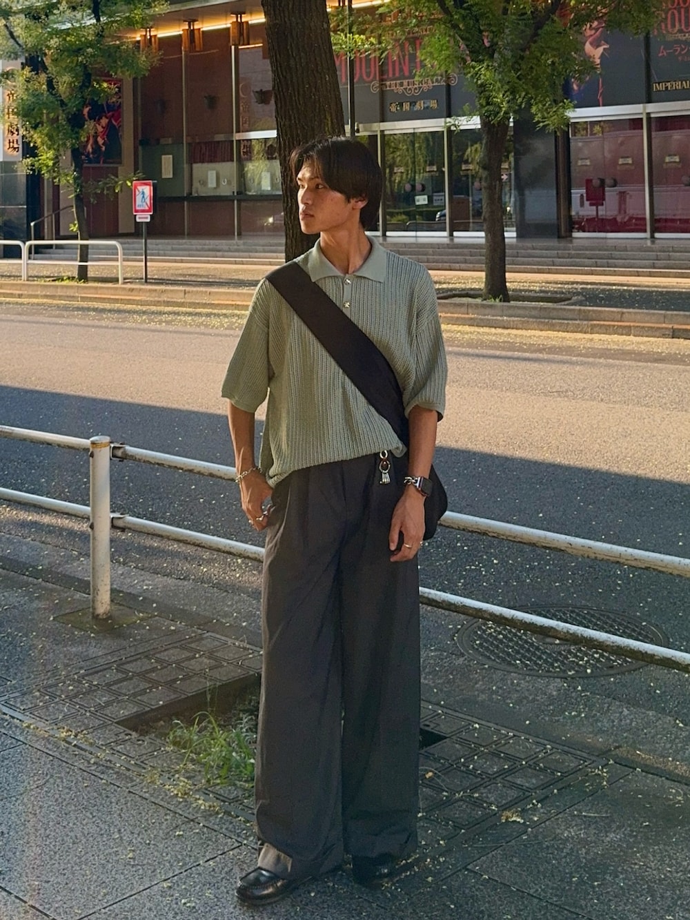 グレー系のスラックス、グリーン系のポロシャツ、ブラック系のショルダーバッグを着用したメンズの夏コーディネートの3枚目の写真