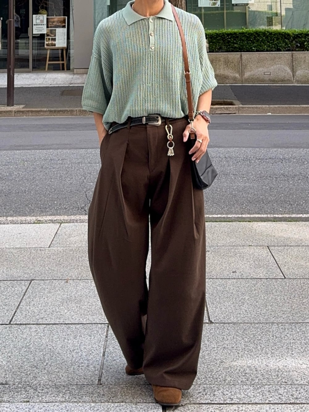 グリーン系のポロシャツ、ブラウン系のスラックス、ブラック系のショルダーバッグを着用したメンズの春コーディネートの4枚目の写真