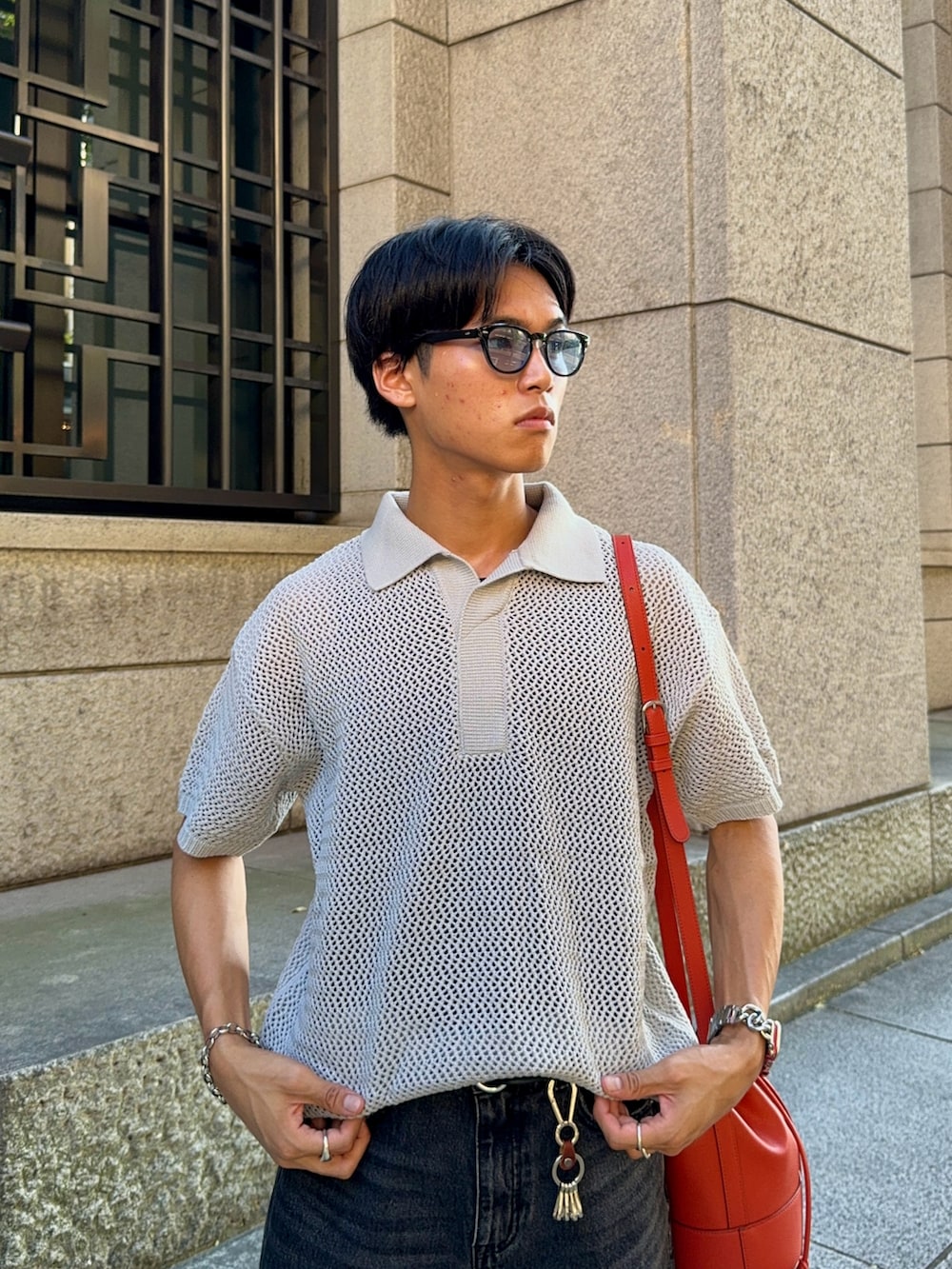 ブラック系のデニムパンツ、グレー系のポロシャツ、オレンジ系のバッグを着用したメンズの夏コーディネートの2枚目の写真