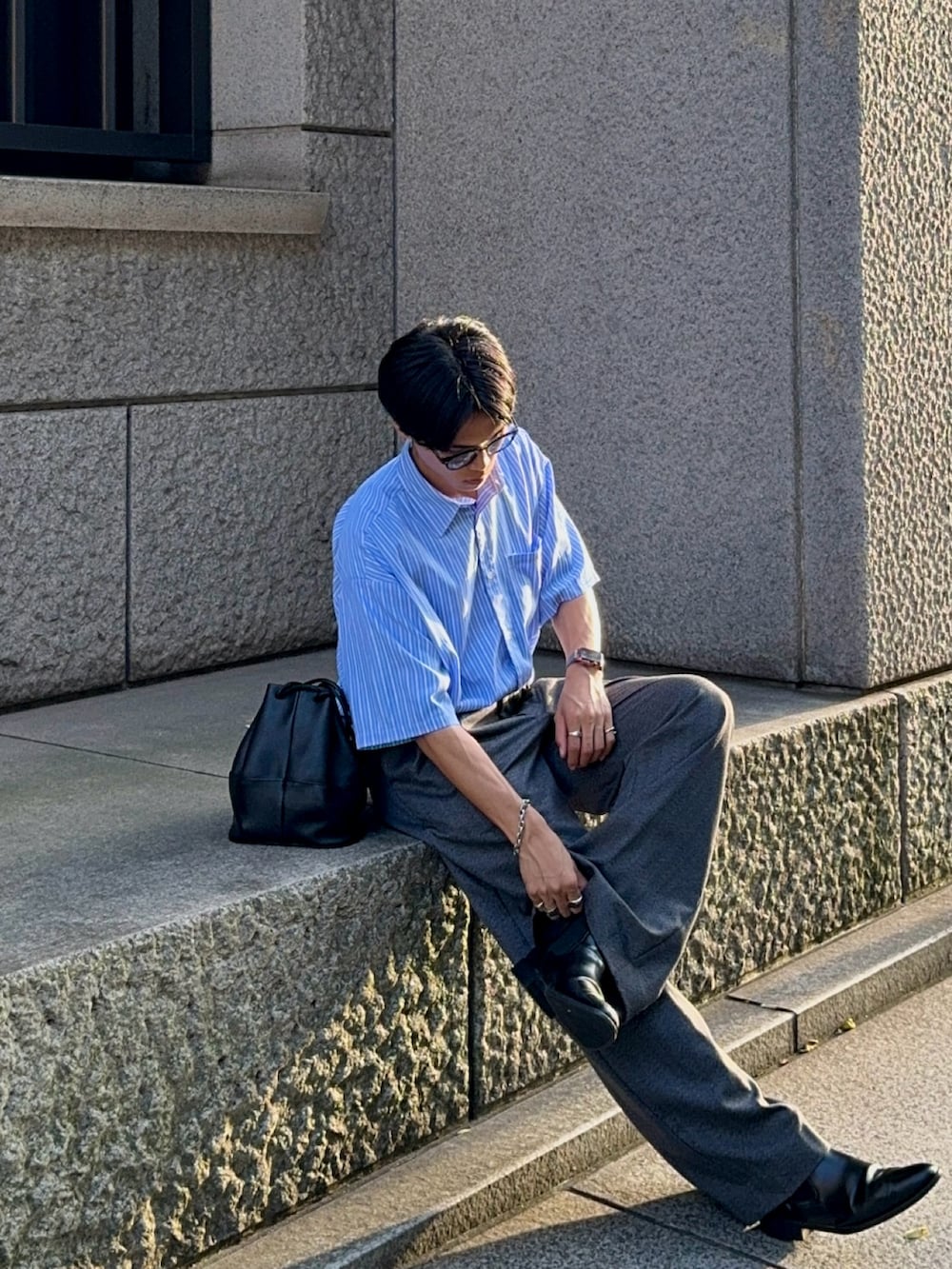 グレー系のスラックス、ブラック系のバッグ、ブルー系のシャツ/ブラウスを着用したメンズの夏コーディネートの3枚目の写真