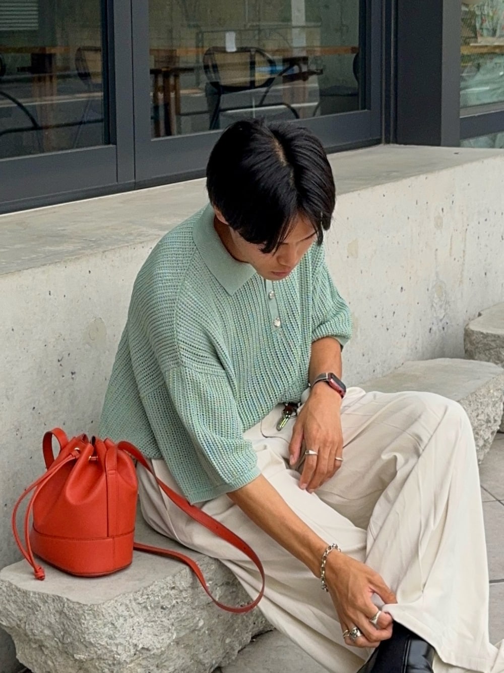 グリーン系のポロシャツ、オレンジ系のバッグ、ホワイト系のスラックスを着用したメンズの夏コーディネートの2枚目の写真