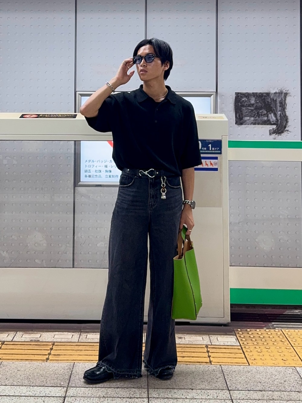 ブラック系のポロシャツ、ブラック系のデニムパンツ、グリーン系のハンドバッグを着用したメンズの夏コーディネートの3枚目の写真