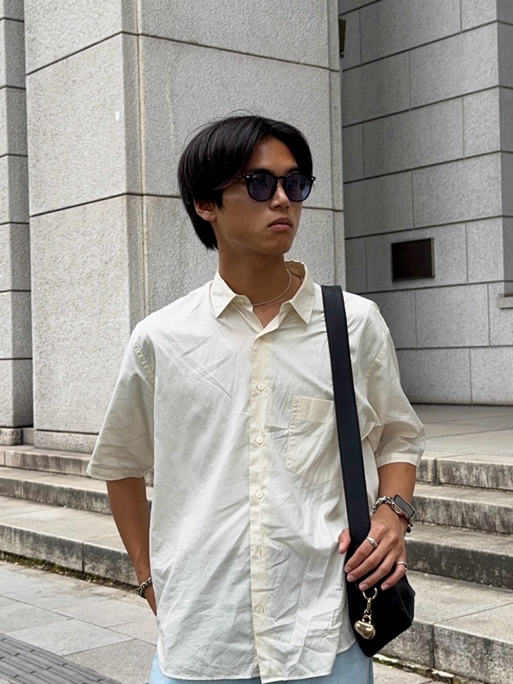 ブラック系のハンドバッグ、ベージュ系のシャツ/ブラウス、ブルー系のデニムパンツを着用したメンズの夏コーディネートの2枚目の写真