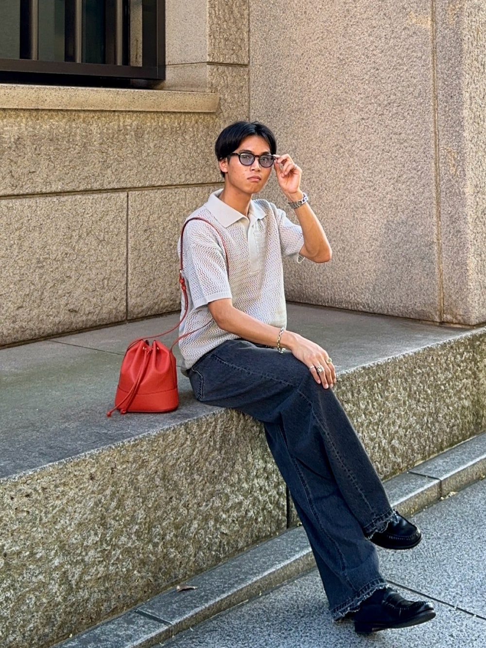 ブラック系のデニムパンツ、グレー系のポロシャツ、オレンジ系のバッグを着用したメンズの夏コーディネートの3枚目の写真