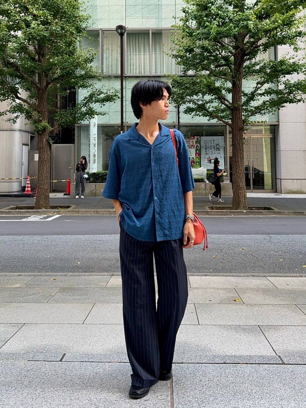 ブルー系のシャツ/ブラウス、オレンジ系のバッグ、ブラック系のスラックスを着用したメンズの夏コーディネートの3枚目の写真