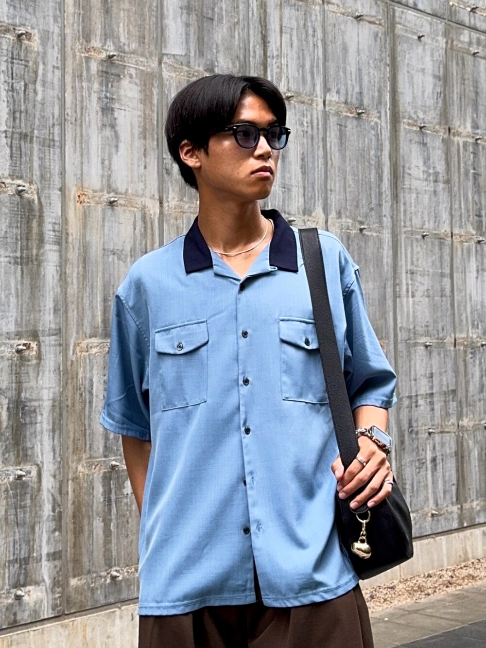 ブルー系のシャツ/ブラウス、ブラック系のハンドバッグ、ブラウン系のスラックスを着用したメンズの春コーディネートの2枚目の写真