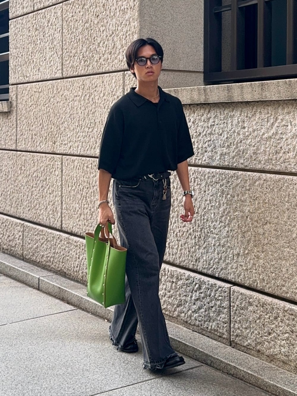 ブラック系のポロシャツ、ブラック系のデニムパンツ、グリーン系のハンドバッグを着用したメンズの夏コーディネートの5枚目の写真