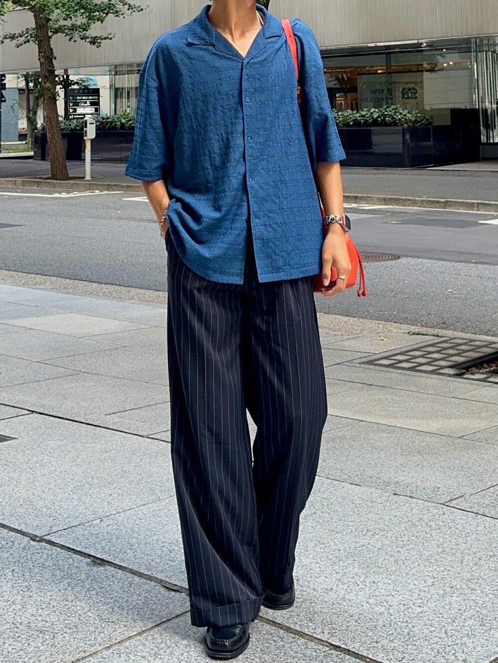 ブルー系のシャツ/ブラウス、オレンジ系のバッグ、ブラック系のスラックスを着用したメンズの夏コーディネートの4枚目の写真