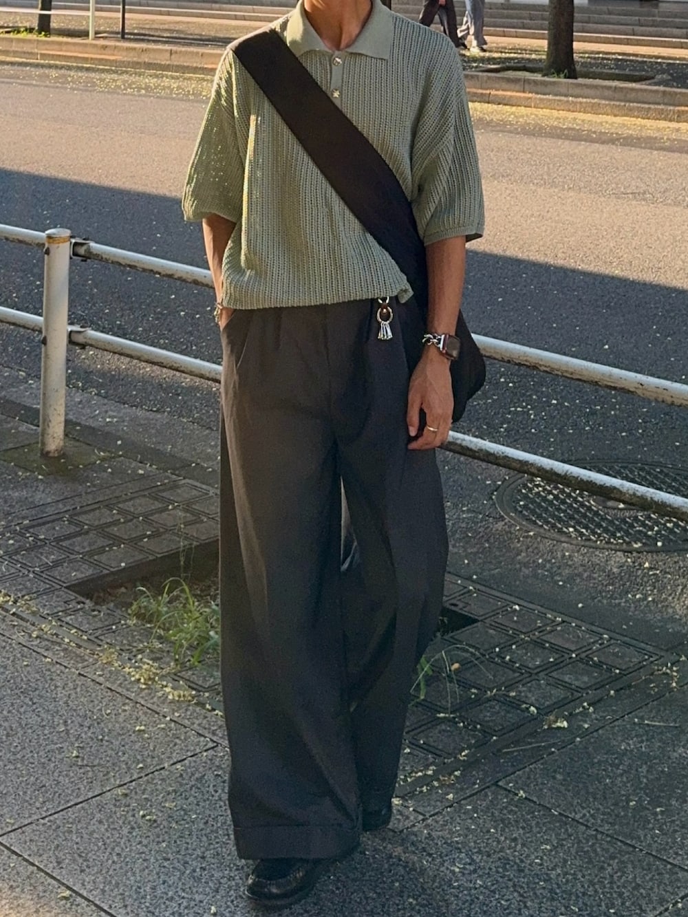 グレー系のスラックス、グリーン系のポロシャツ、ブラック系のショルダーバッグを着用したメンズの夏コーディネートの4枚目の写真