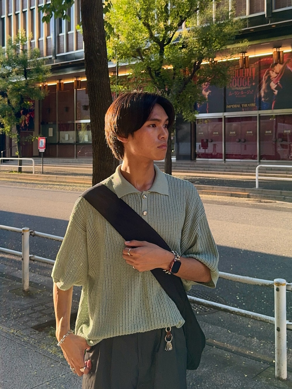 グレー系のスラックス、グリーン系のポロシャツ、ブラック系のショルダーバッグを着用したメンズの夏コーディネートの2枚目の写真